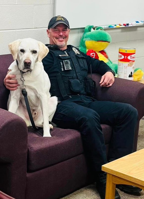 Officer Ogle sits on a couch with K9 Toro