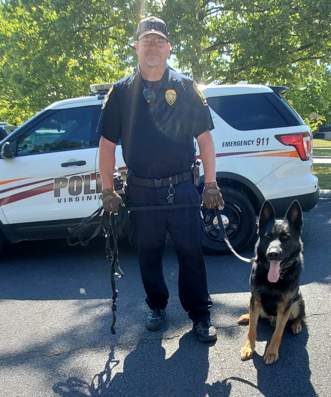 Officer Reece stands next to a sitting K9 Zuka in a parking lot