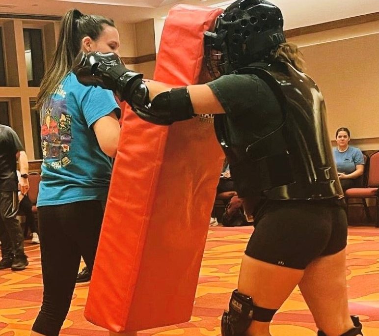 A female with protective gear hits a RAD red bag held by a female instructor.